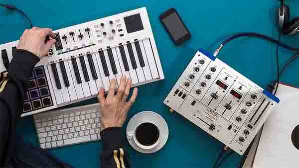 getting-music-for-your-song Person Playing a Midi Keyboard Next to a Mixer